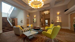 A spacious lobby with a modern chandelier, a staircase, and a seating area with yellow chairs.