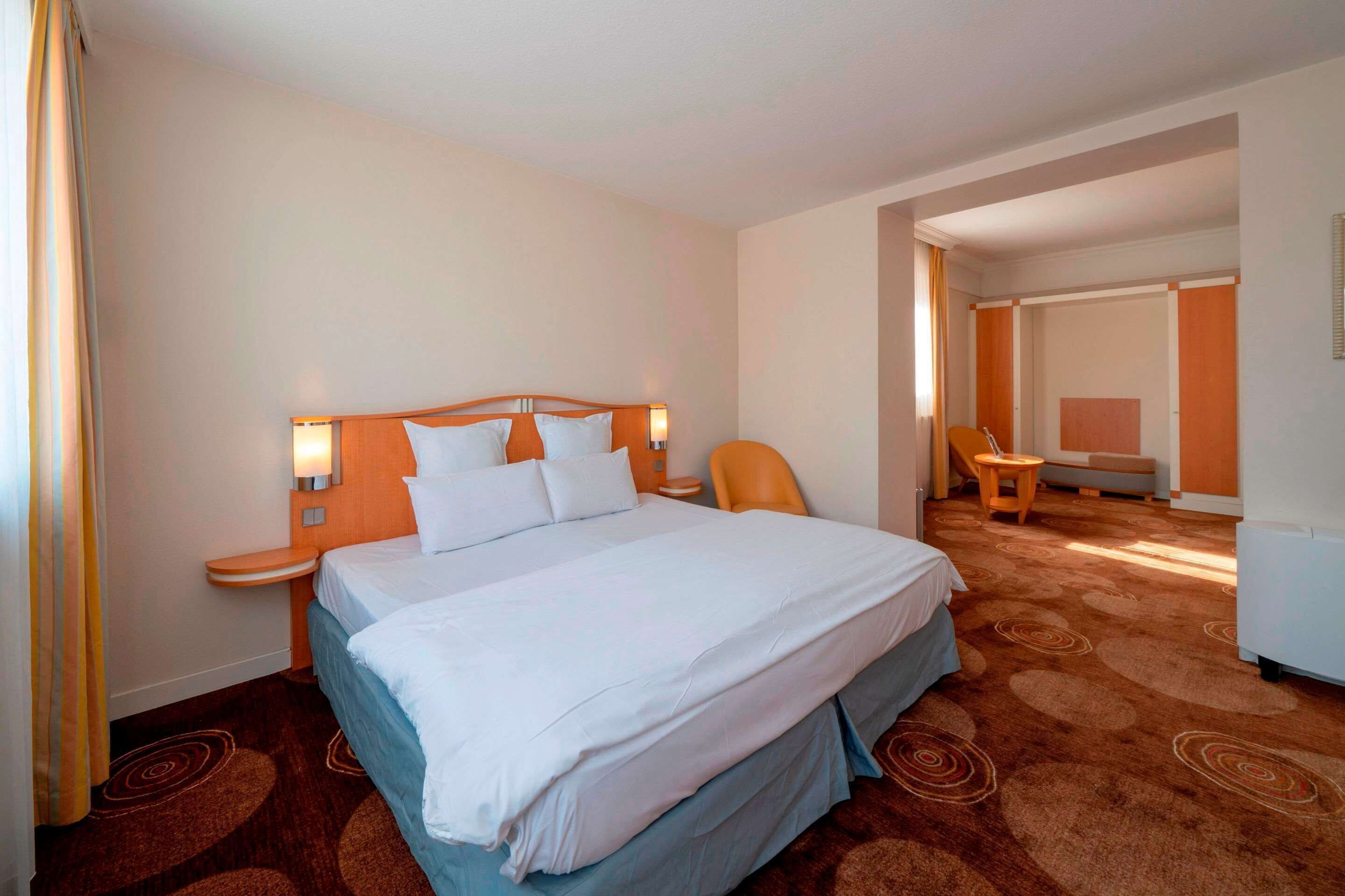 Une chambre d’hôtel avec un grand lit, une tête de lit en bois, une table de chevet, une chaise et un bureau.
