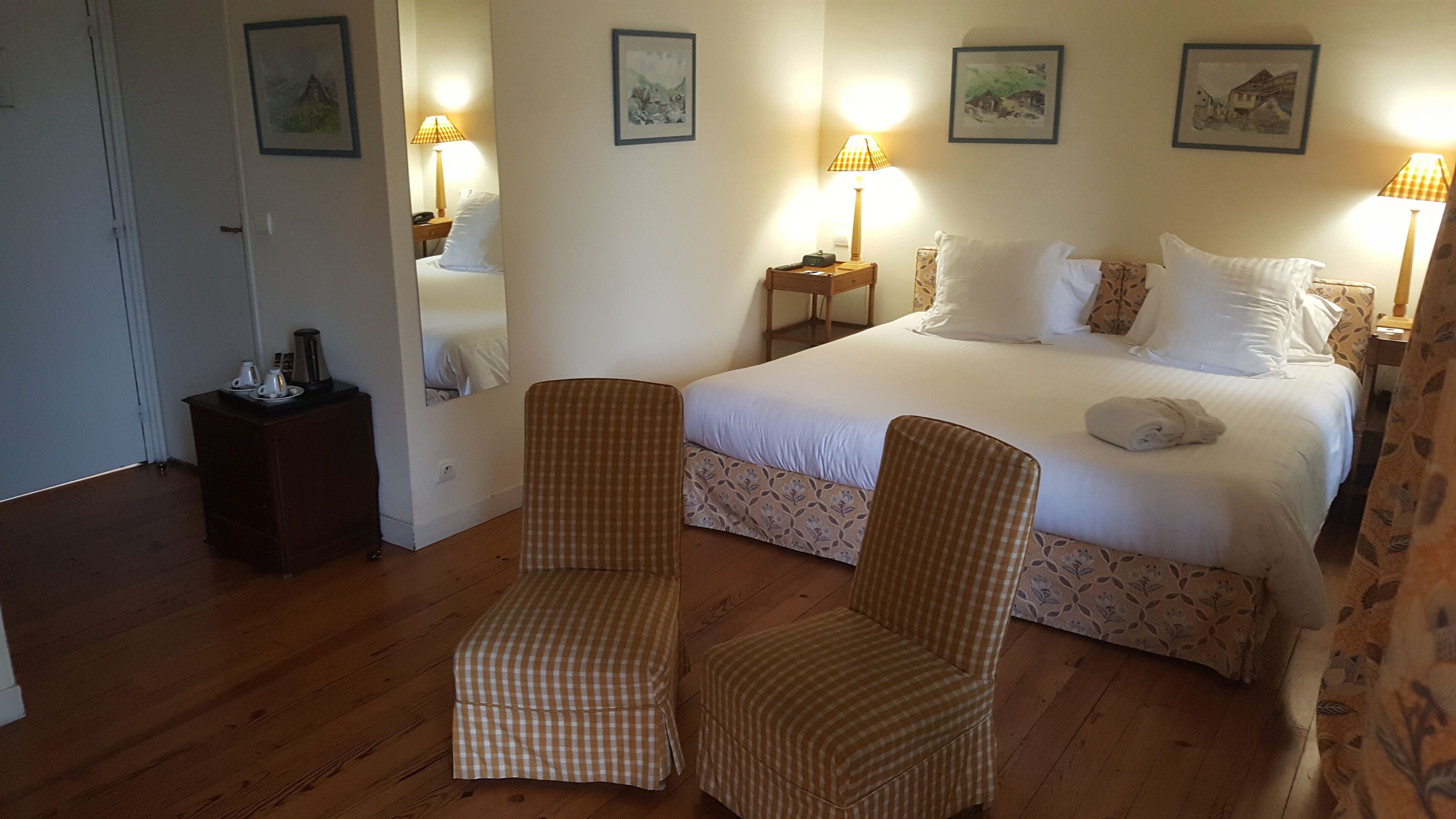 A hotel room with a large bed, two armchairs, a bedside table with a lamp, and framed pictures on the wall.