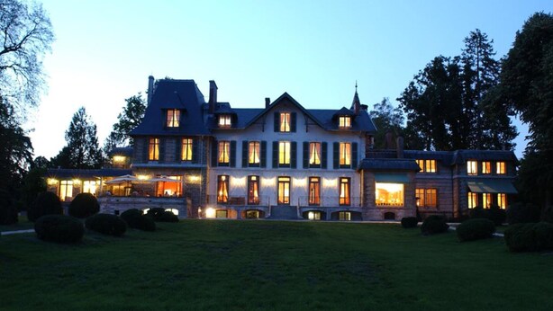 A large, multi-story building with a symmetrical facade, multiple windows, and a well-maintained lawn.