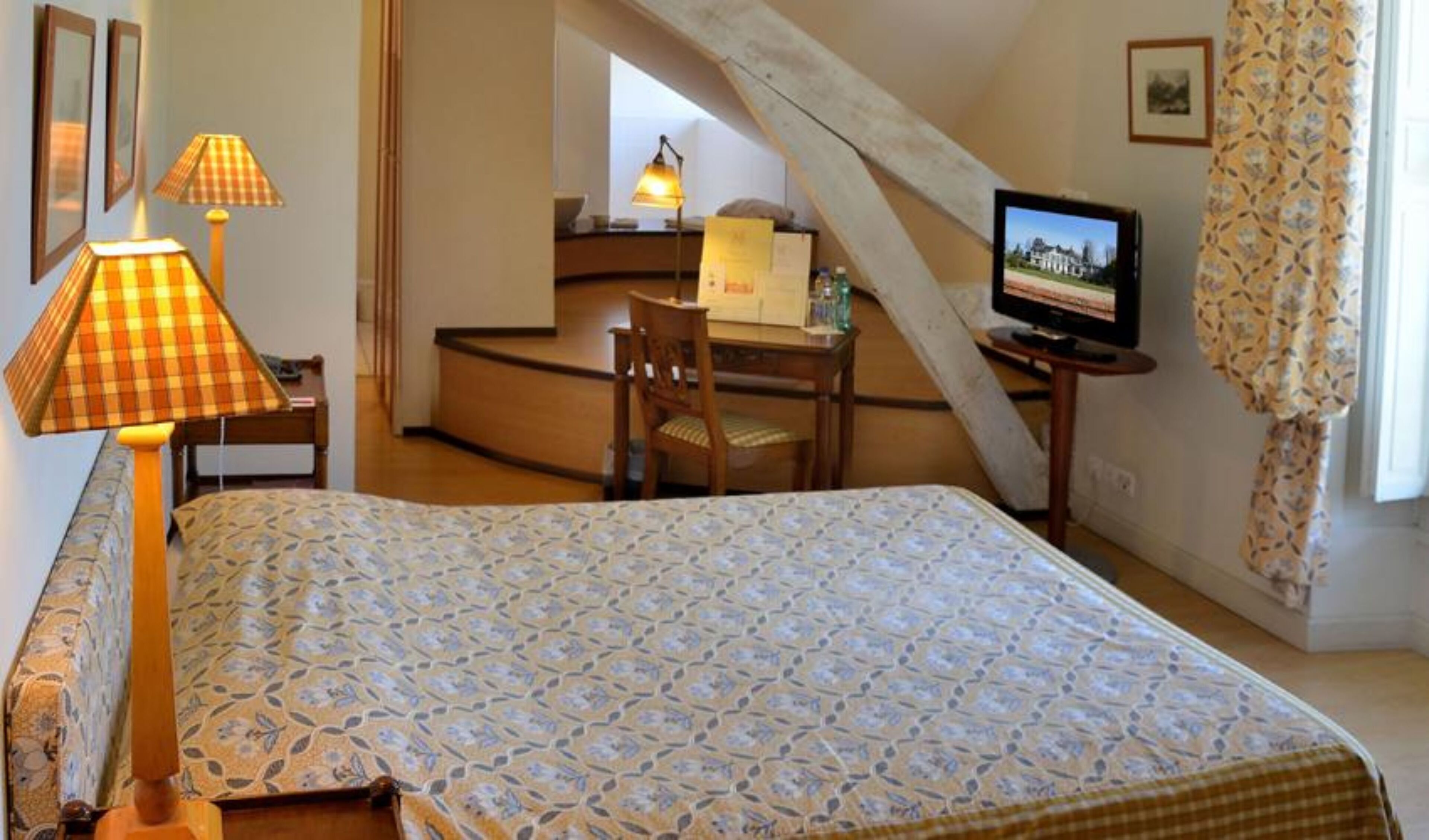 A bedroom with a bed, a desk, a chair, a television, and a window with curtains.