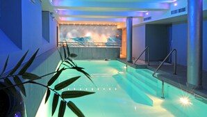 A modern indoor swimming pool with a view of a mountain landscape through a glass wall, surrounded by a minimalist design with blue lighting.