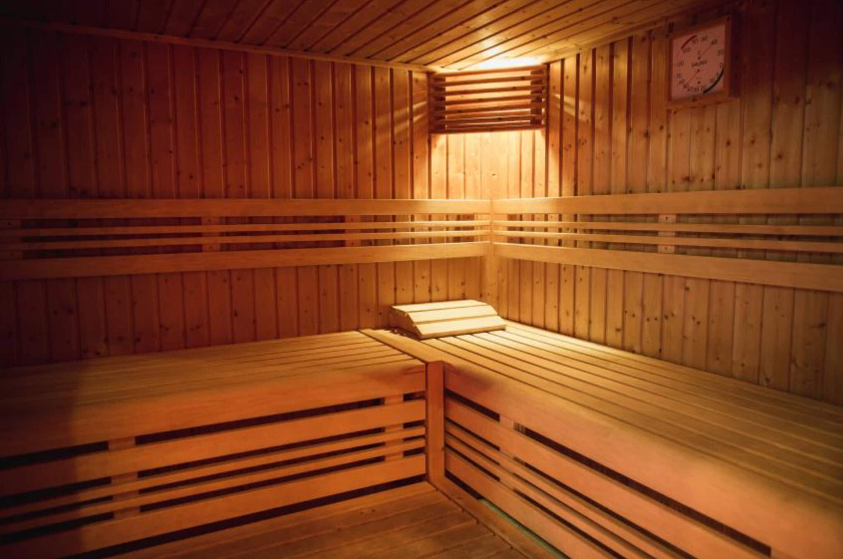 A sauna with wooden benches and slatted seats, wooden walls, and a visible thermometer on the wall.