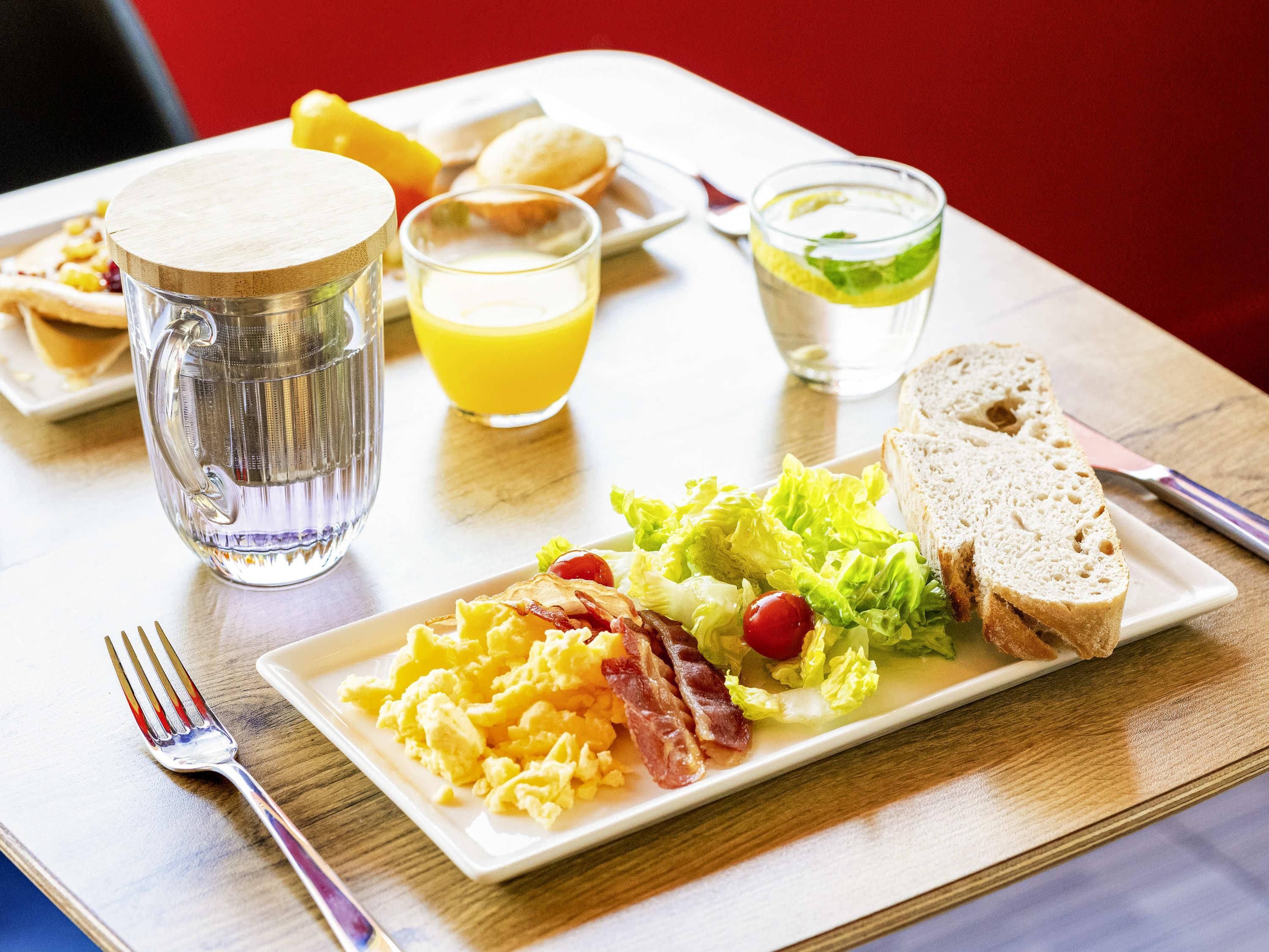 En morgenmadstallerken med røræg, bacon og salat, samt ristet brød og appelsinjuice.