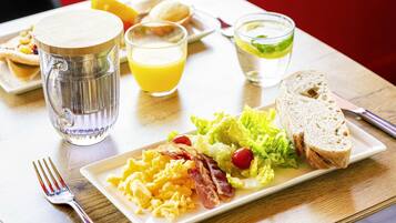 En morgenmadstallerken med røræg, bacon og salat, samt ristet brød og appelsinjuice.