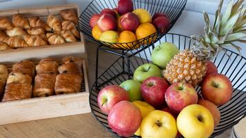 A kitchen counter with a fruit bowl containing apples, oranges, and a pineapple, and a wooden box with pastries.