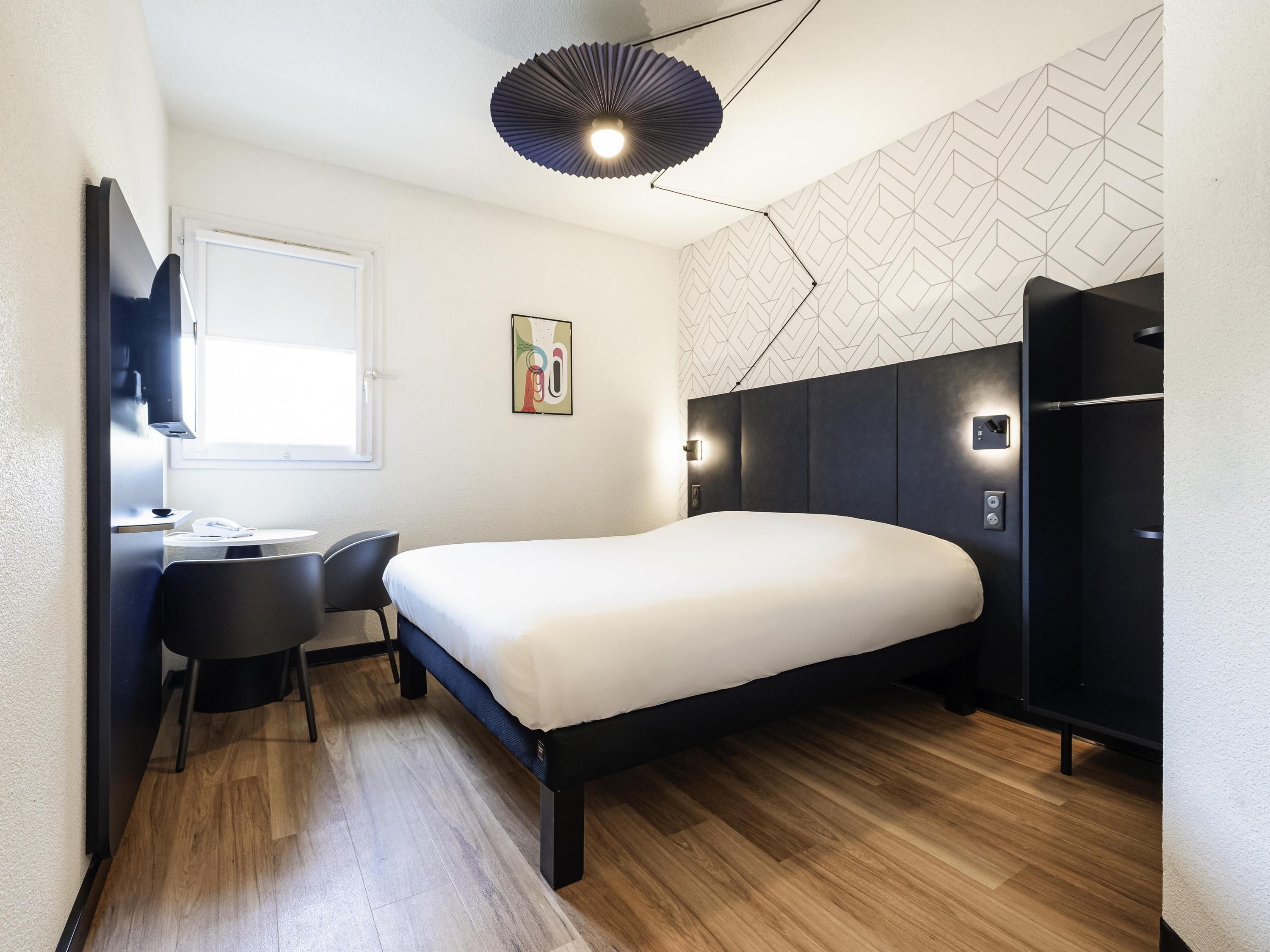 Une chambre d’hôtel moderne équipée d’un lit, d’un bureau, d’une chaise et d’un luminaire au plafond au design original.