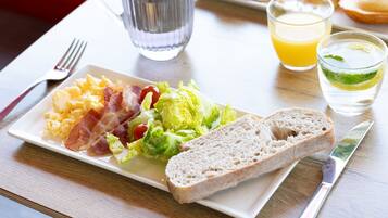 A breakfast plate with scrambled eggs, bacon, lettuce, and toast, accompanied by a glass of orange juice and a glass of water with a slice of lime.