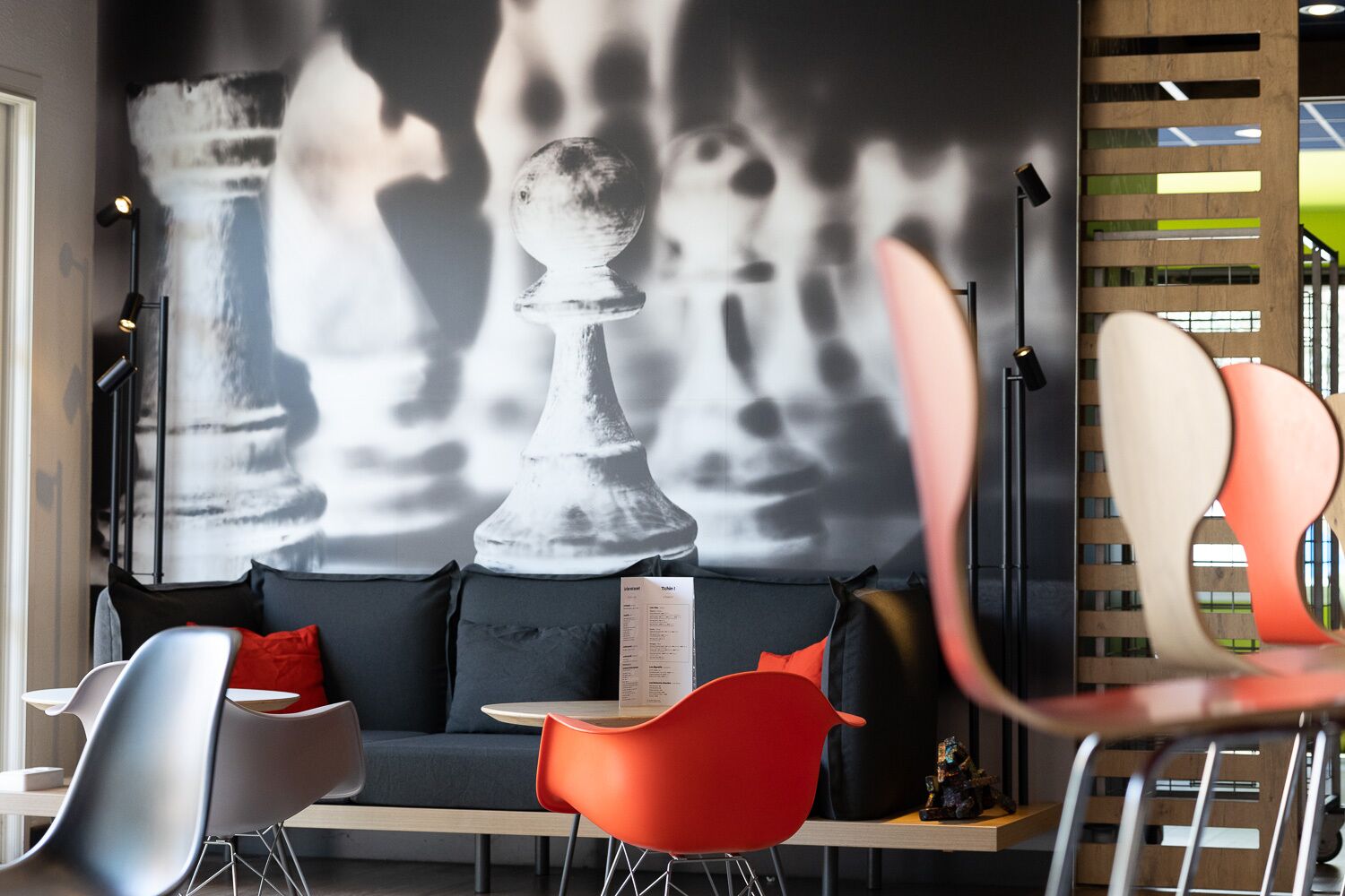 Un intérieur moderne avec un canapé, deux fauteuils rouges et une fresque représentant un jeu d’échecs sur le mur.