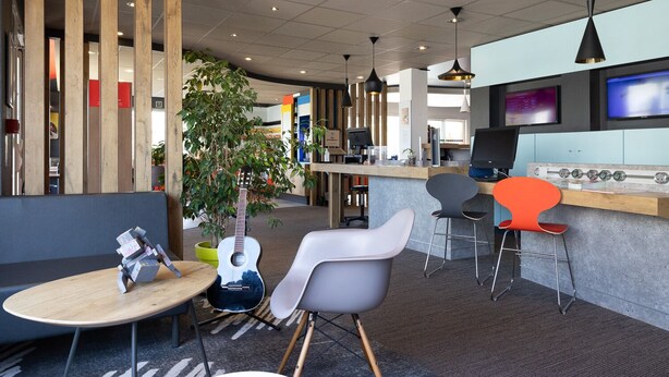 Un espacio de oficina moderno con un mostrador de recepción, múltiples monitores de computadora y diversas opciones de asiento, incluyendo una mesa redonda, una silla blanca y una silla roja.