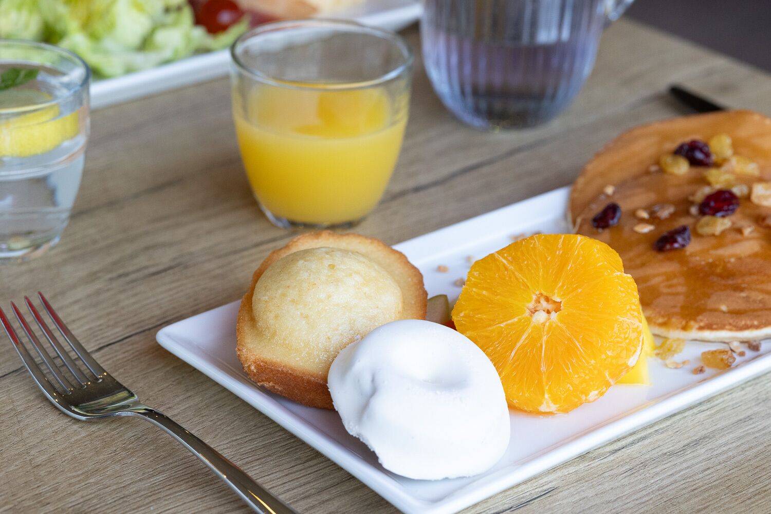 Une assiette de petit-déjeuner avec un muffin, une boule de glace et une tranche d’orange, le tout présenté sur une assiette blanche.