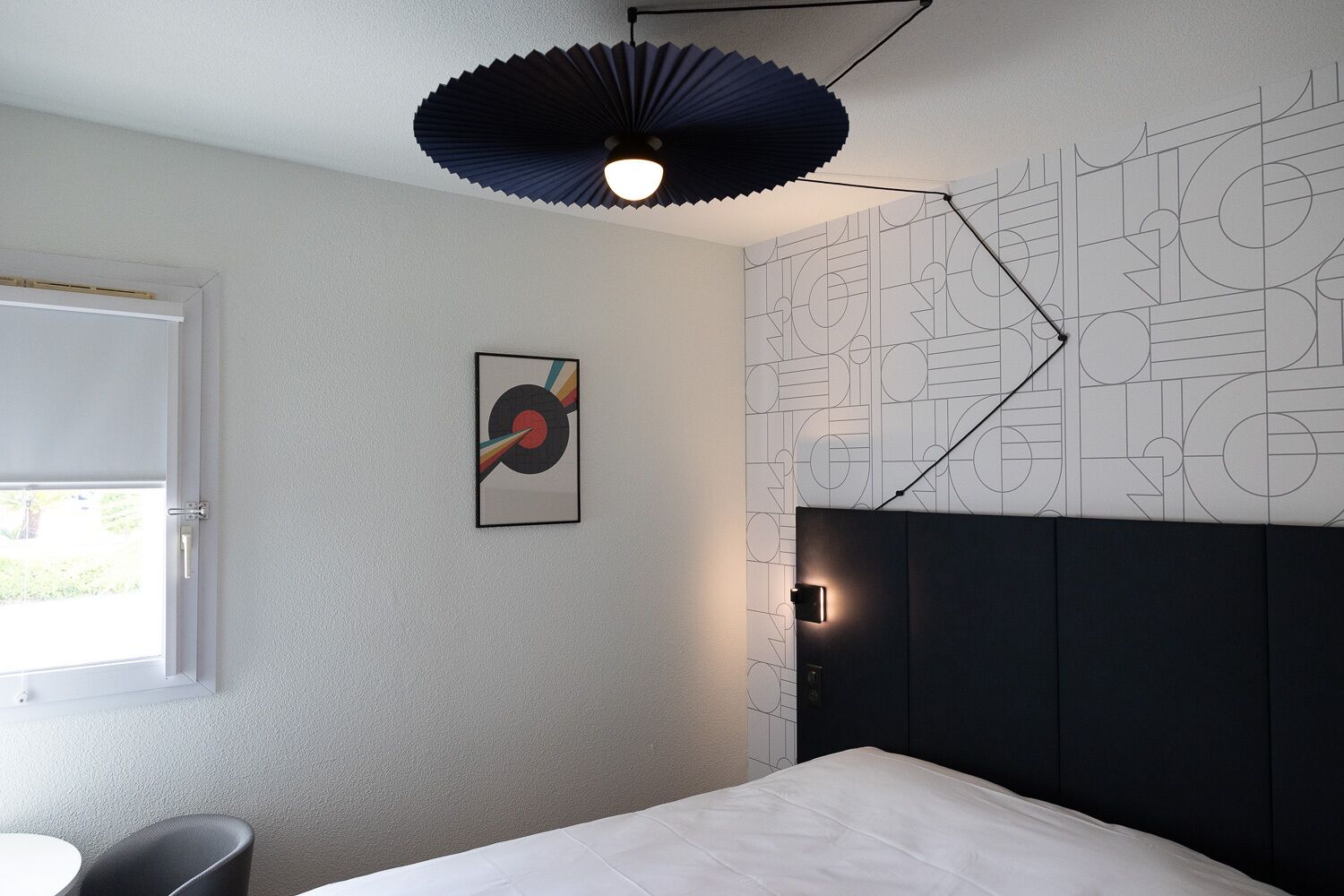 Een moderne slaapkamer met een bed, een wandlamp en een muur met een geometrisch patroon.