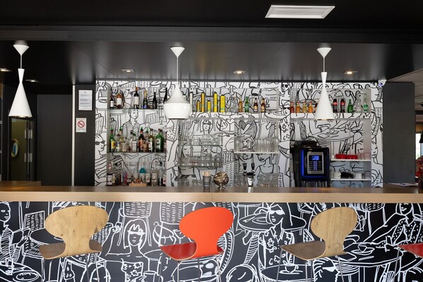 A bar area with a black and white mural, shelves with bottles, and a coffee machine. - ibis Perpignan Sud Saint Charles (Perpignan)