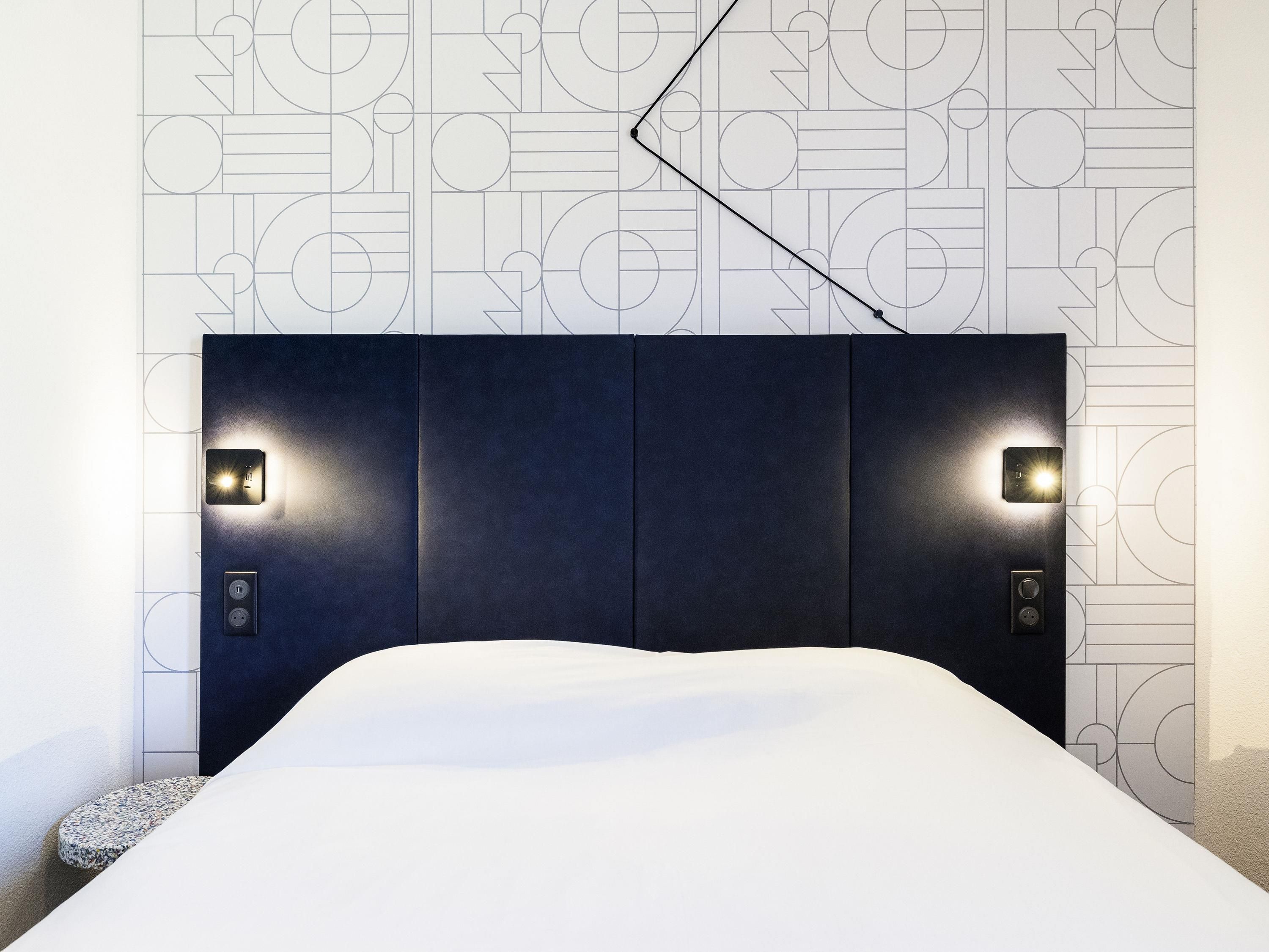 Een moderne hotelkamer met een groot bed, twee wandlampen en een geometrisch patroon op de muur.