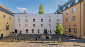 A courtyard with a white building, bicycles, and a car parked nearby.