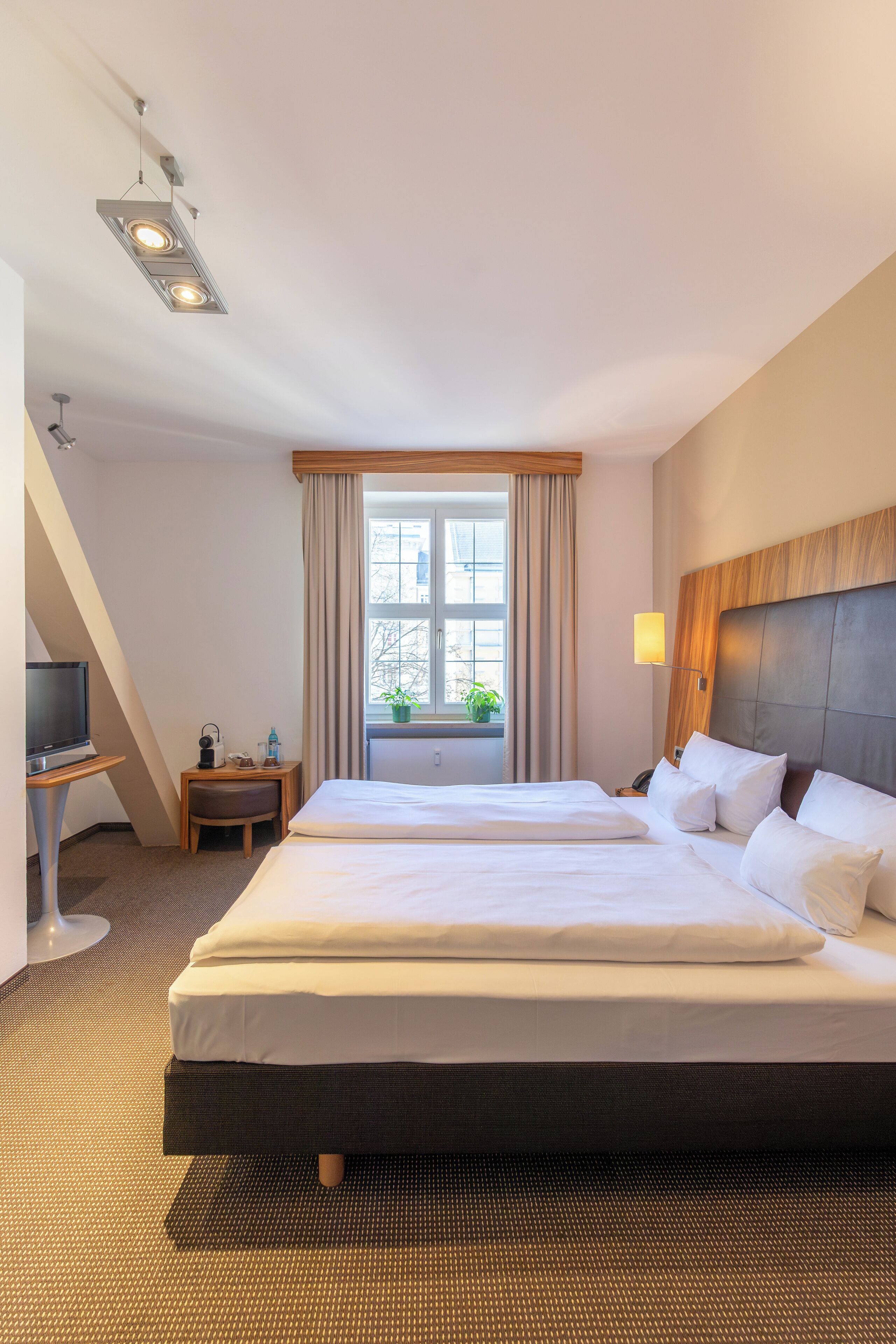 Une chambre d’hôtel avec un grand lit, une télévision posée sur une table d’appoint, une fenêtre avec des rideaux et une lampe sur la table de chevet.
