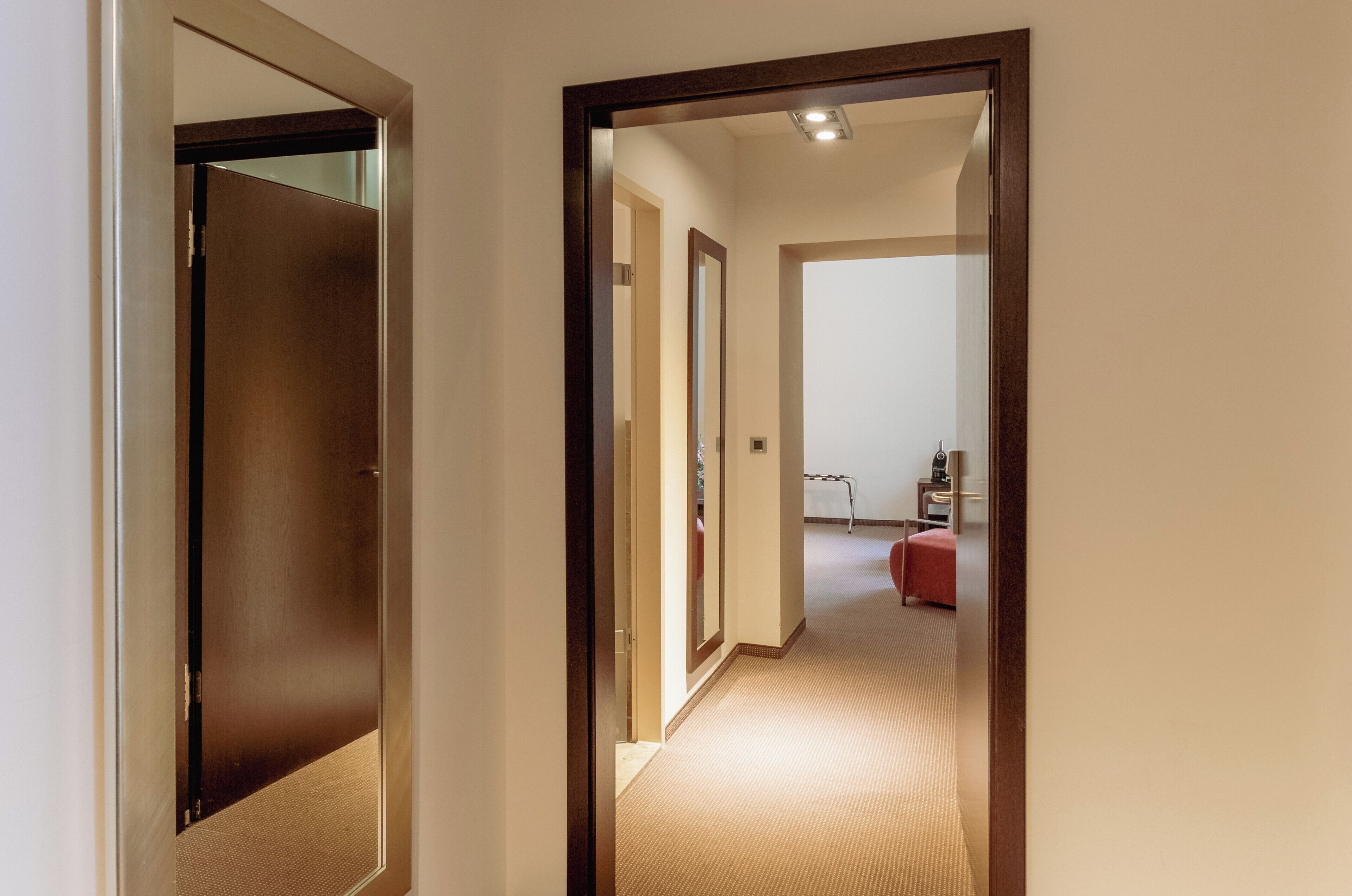 A hallway with a carpeted floor, a wooden door frame, and a red chair in the distance.