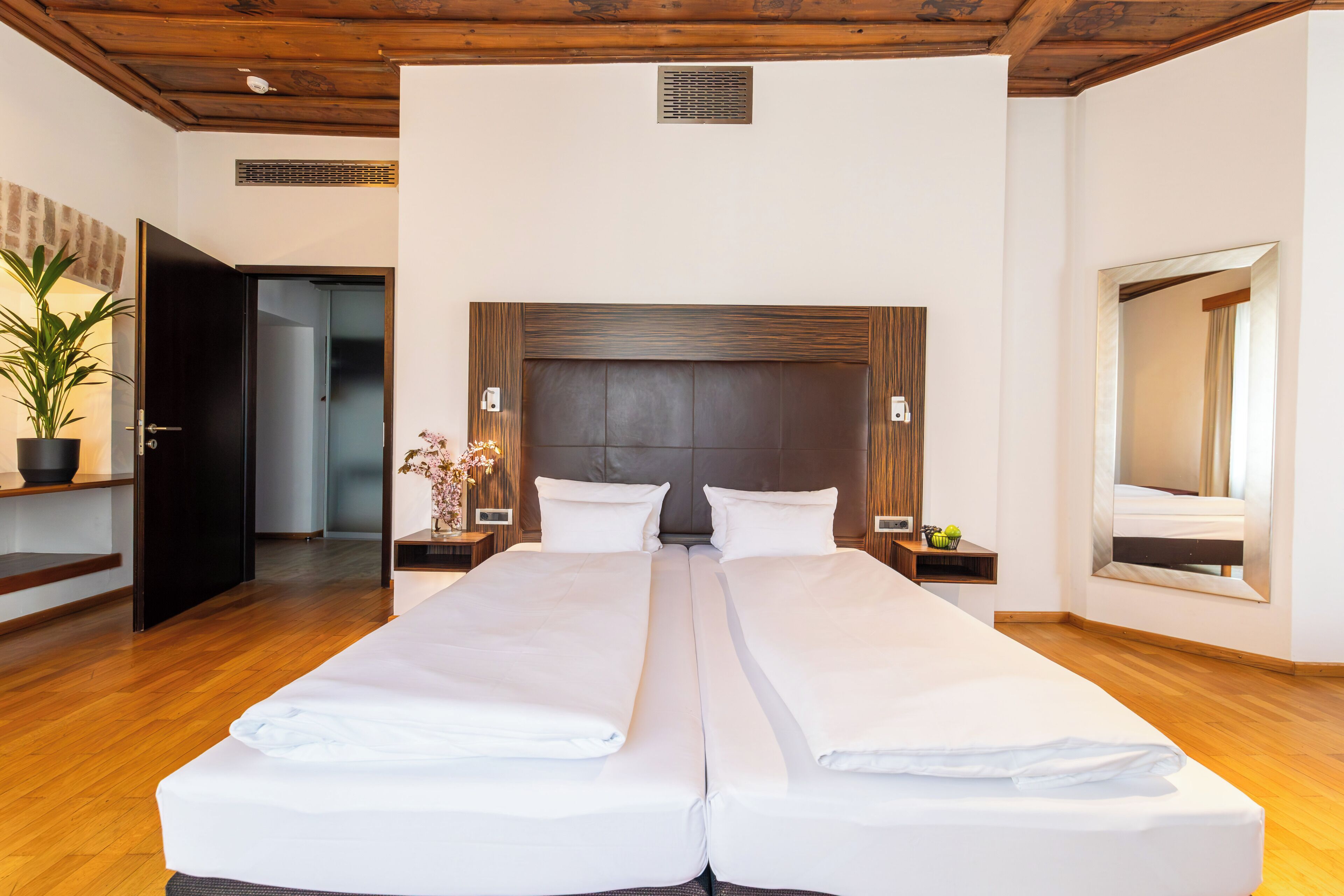 A double bed with a wooden headboard, bedside tables with lamps, a potted plant, and a large mirror on the wall.