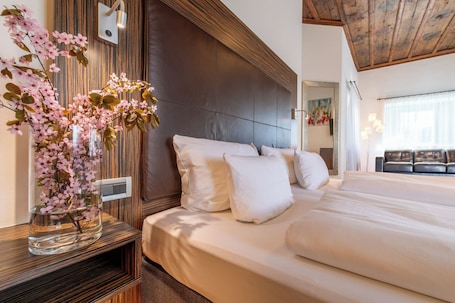A hotel room with a large bed, a wooden headboard, a vase with flowers, and a sofa in the background.