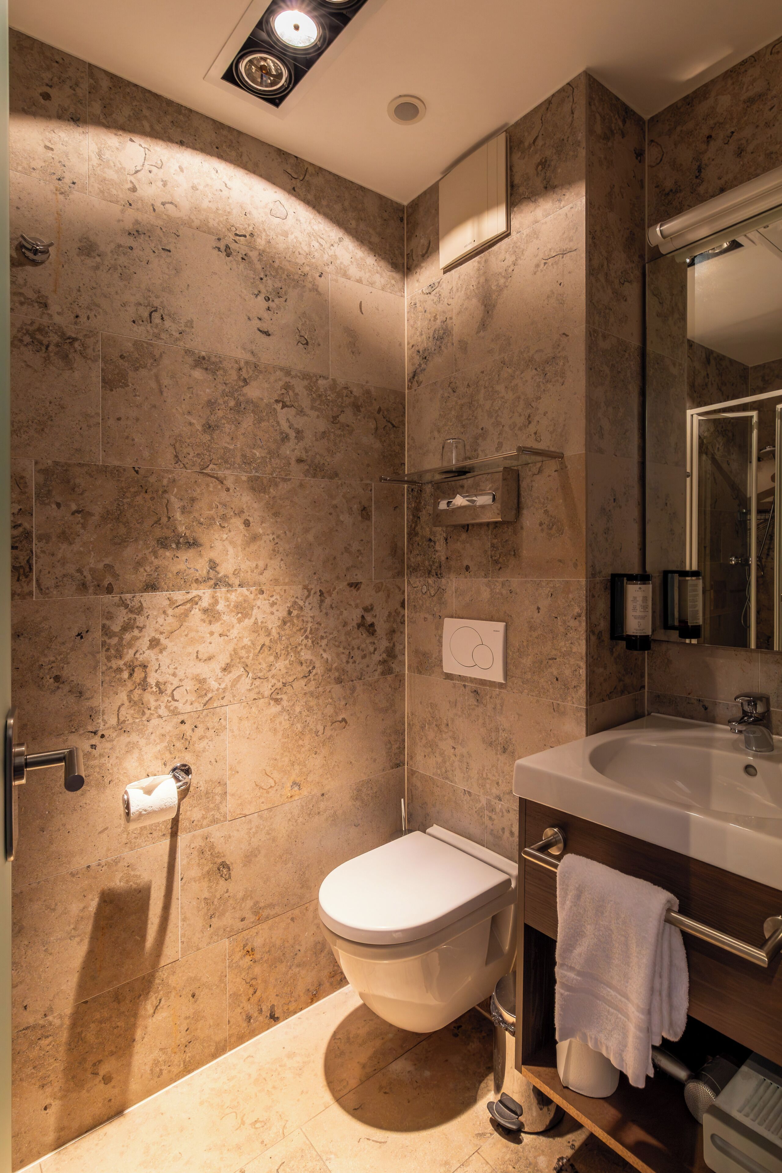 A bathroom with a toilet, sink, mirror, towel rack, and shower area.