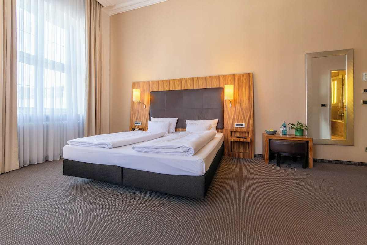 A hotel room with a large bed, two bedside tables, a mirror, and a small table with a plant.