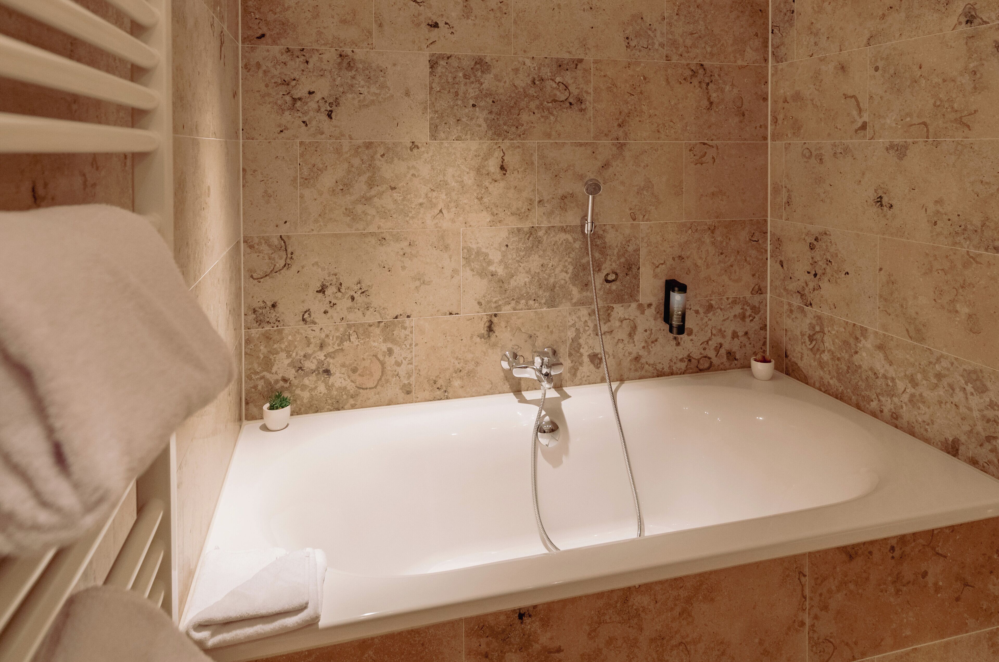 A bathroom with a bathtub, a showerhead, and a small potted plant.