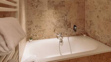 A bathroom with a bathtub, a showerhead, and a small potted plant.