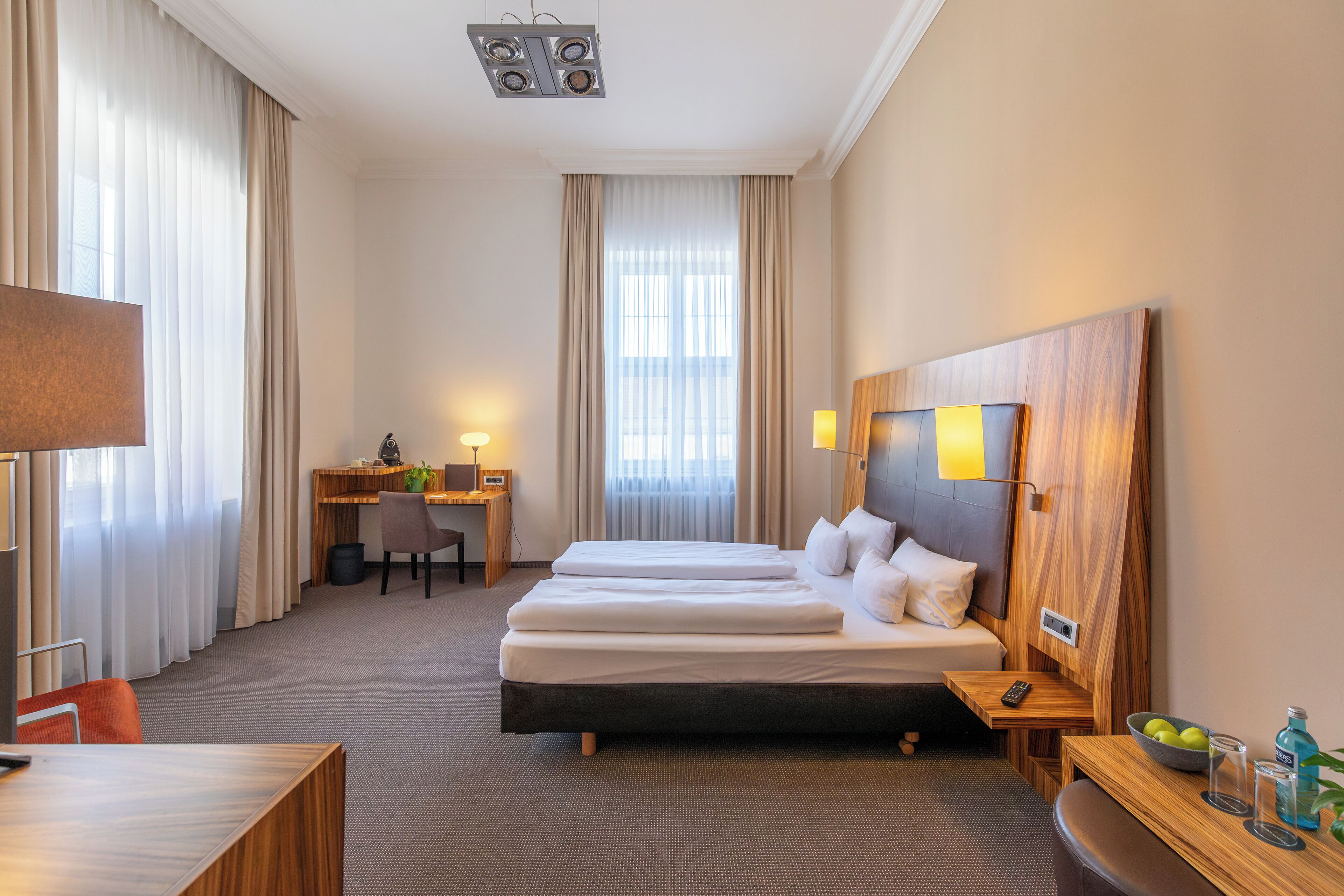 Une chambre d’hôtel avec un lit double, un bureau avec une chaise, une petite table avec un panier de fruits et un téléviseur.