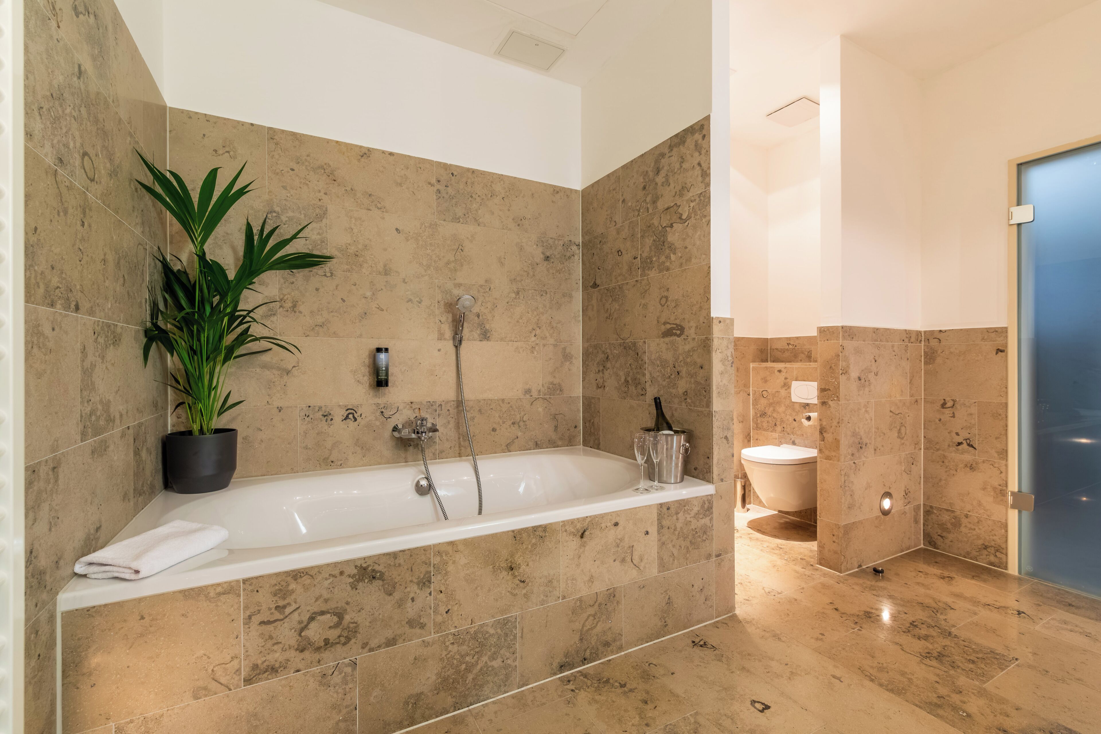 A modern bathroom with a bathtub, a potted plant, and a toilet.