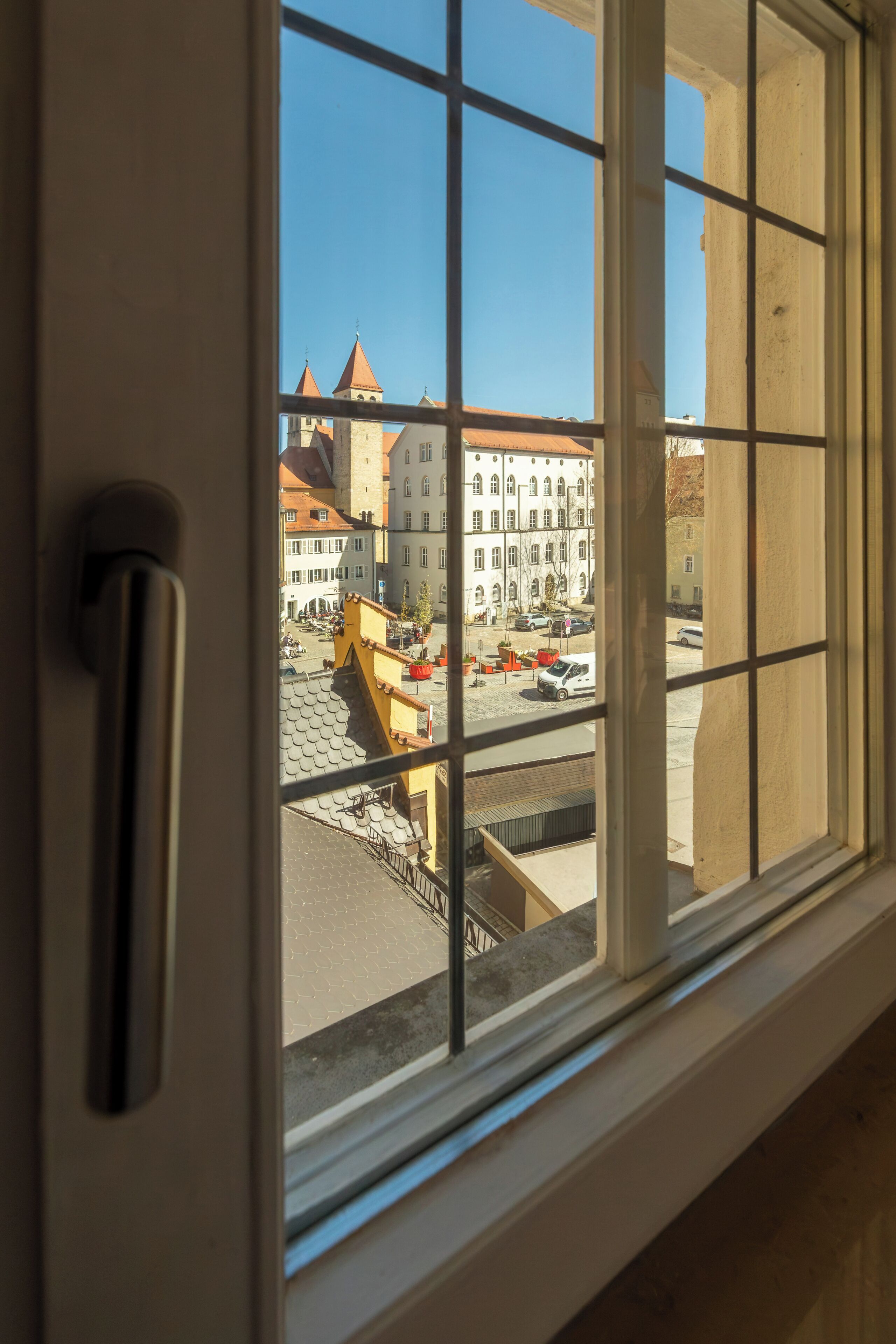 A window with a grid pattern, a door handle, and a view of buildings with a clear sky.