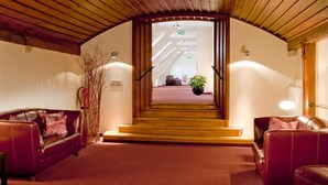 A hotel lobby with a wooden ceiling, a staircase leading to upper floors, and leather sofas with decorative pillows. - Hotel Regensburg Herzogshof am Dom (Regensburg)
