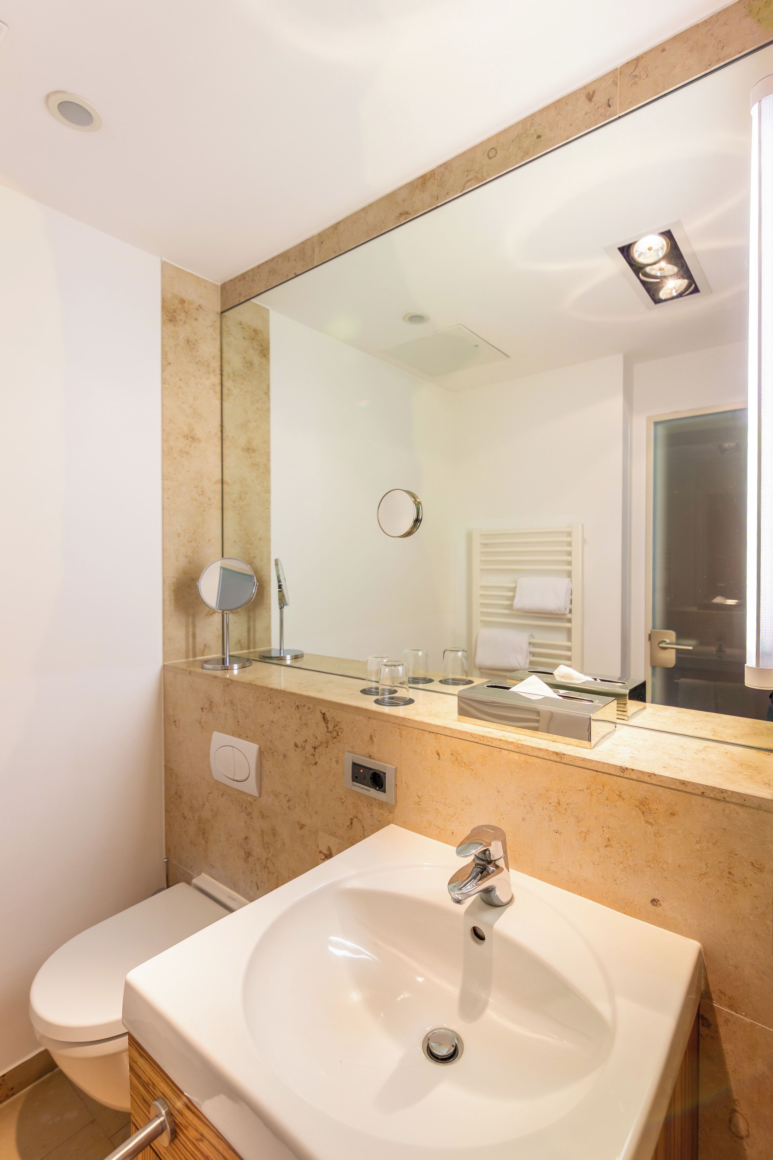 Ein Badezimmer mit einem weißen Waschbecken, einem Spiegel, einem Handtuchhalter und einer Toilette.