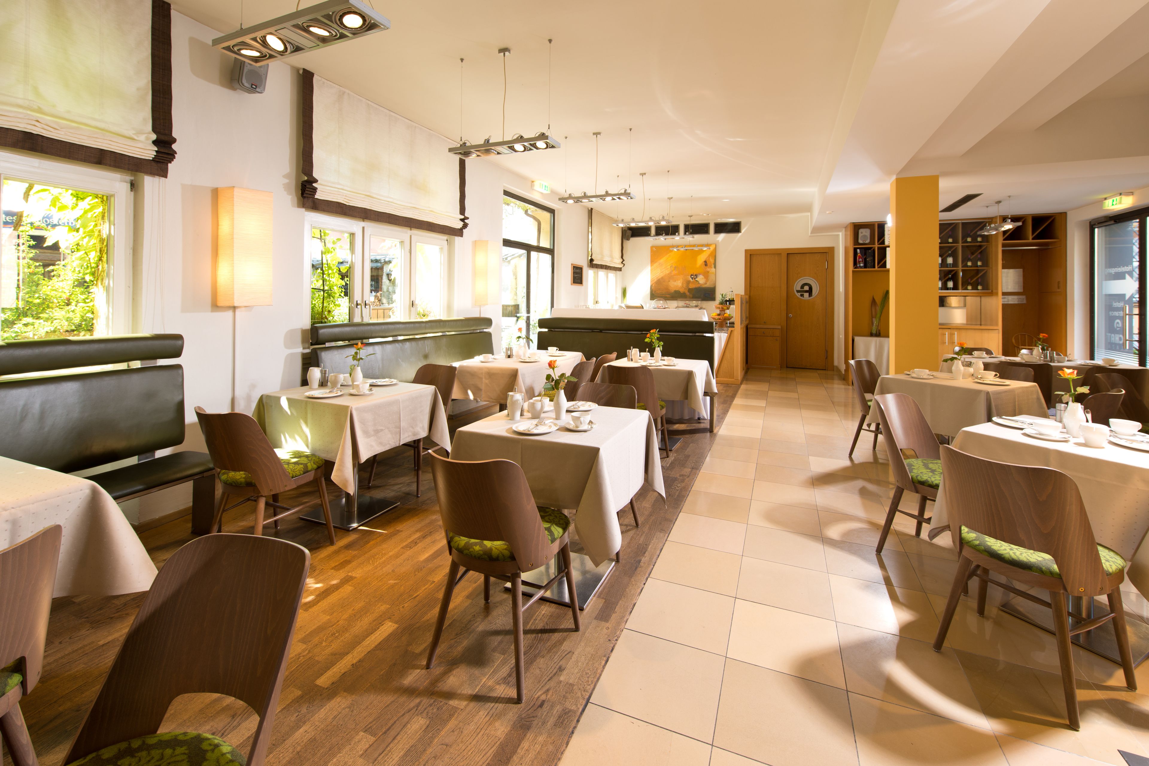 A restaurant with multiple tables and chairs, wooden flooring, and large windows allowing natural light.
