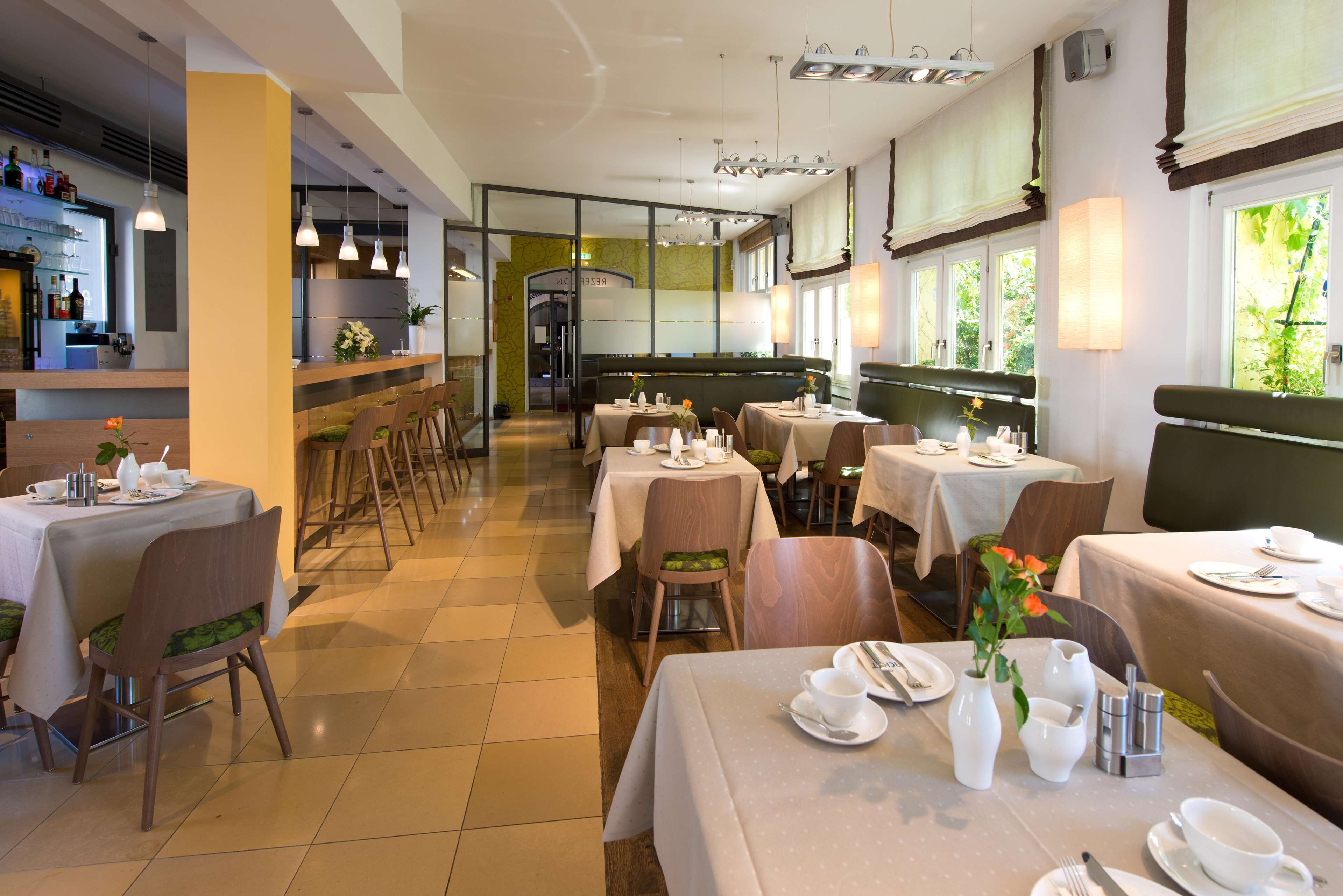 Ein Restaurant mit mehreren Tischen, einer Bar und großen Fenstern, die für natürliches Licht sorgen.