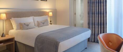 A hotel room with a large bed, two bedside lamps, a chair, and a door leading to a bathroom.