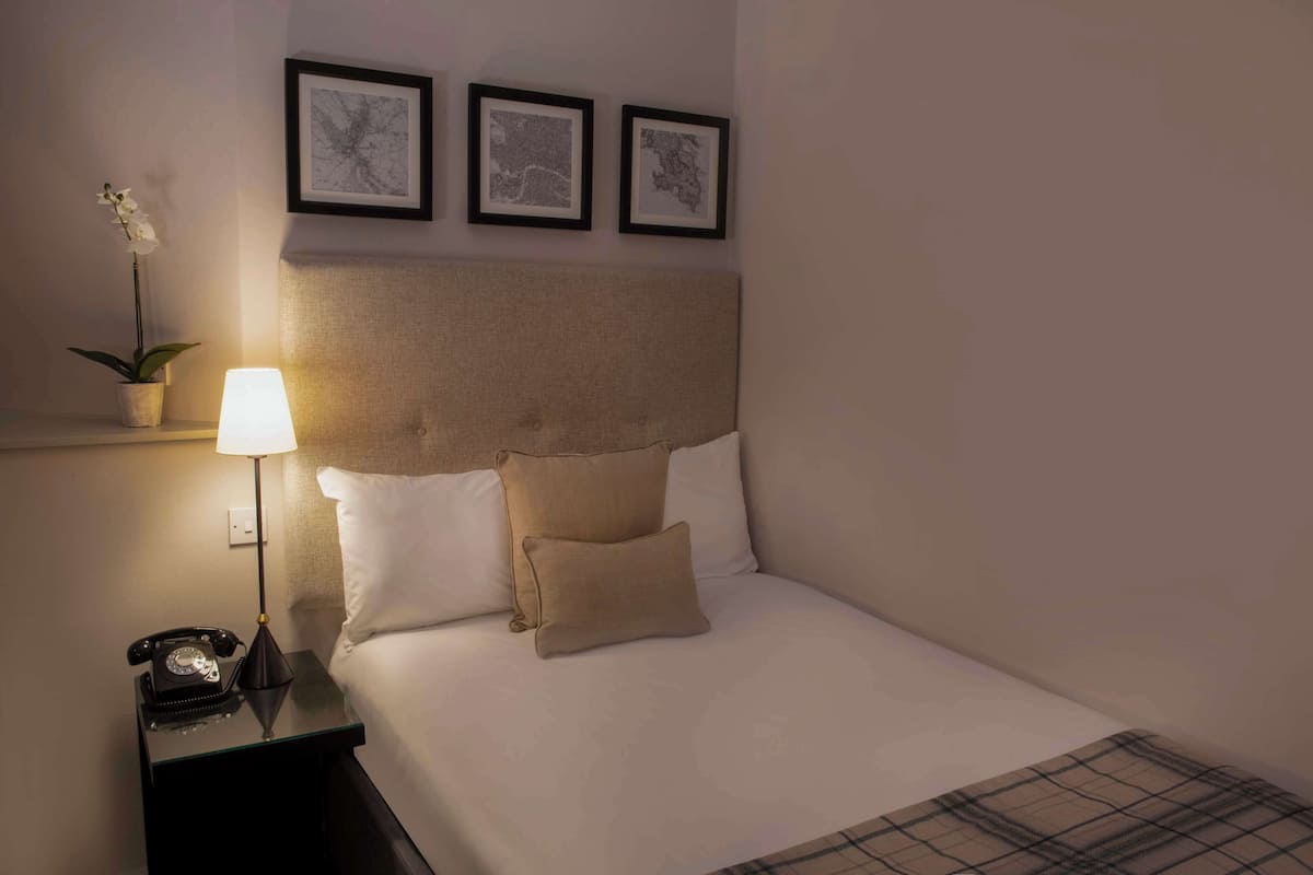A neatly made bed with a headboard, a bedside lamp, a telephone, and a small potted plant.
