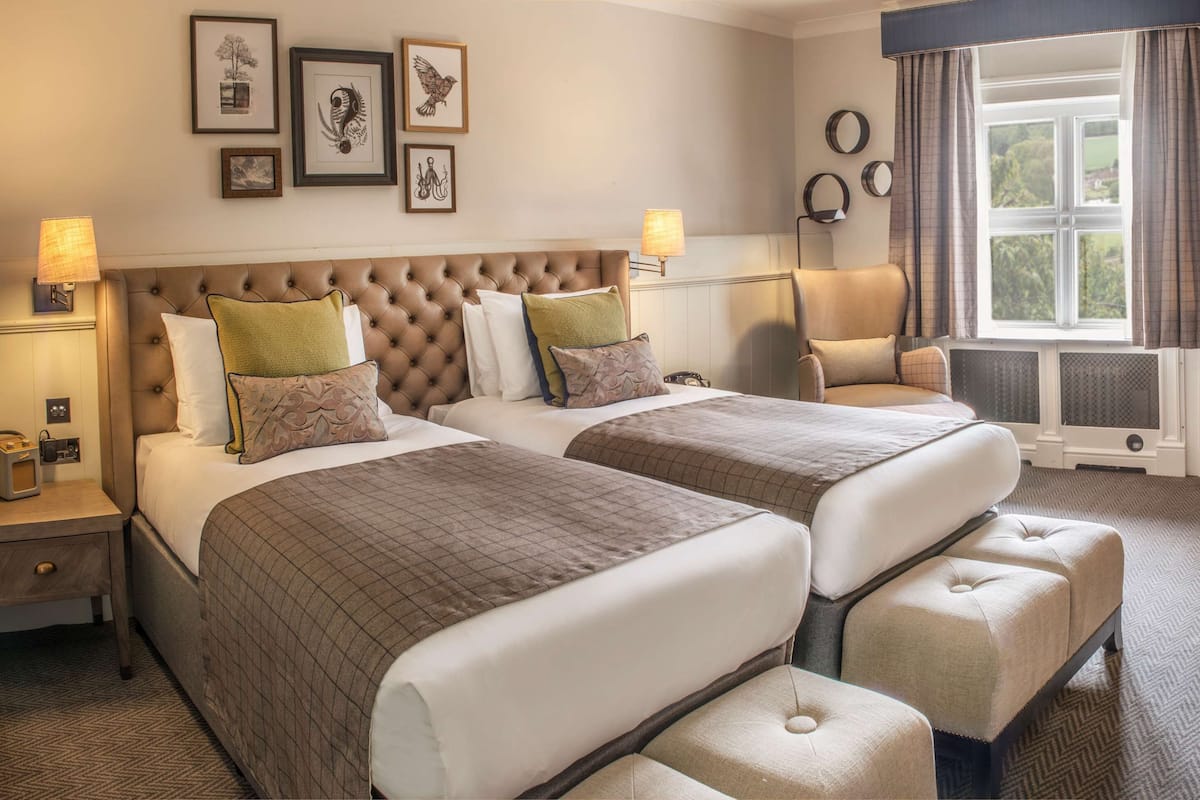 A hotel room with two beds, a sitting area, and a view of the outdoors.