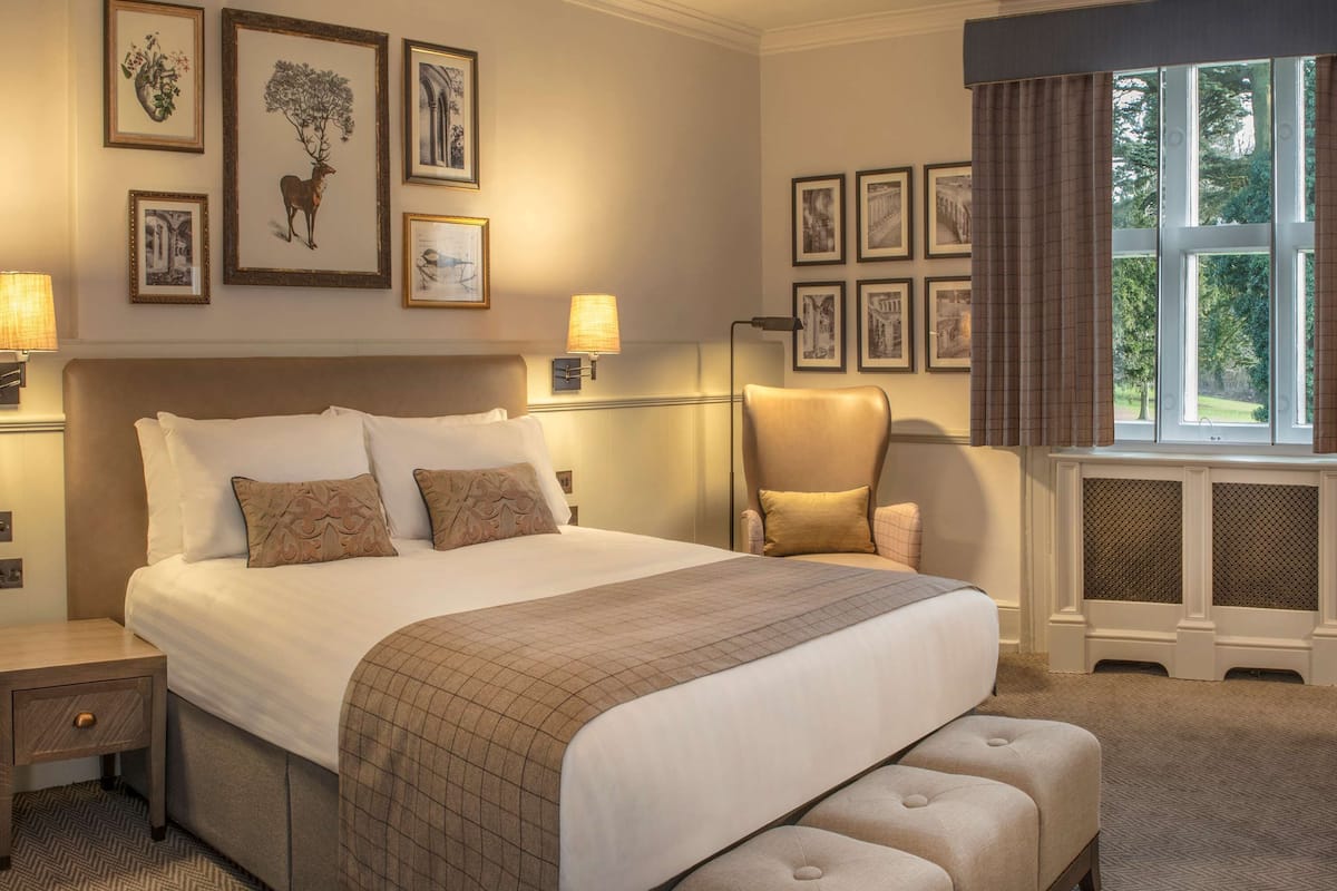 A well-appointed hotel room with a large bed, a seating area with a chair and a table, and a window with curtains.