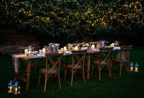 An outdoor dining setup with tables, chairs, candles, and string lights against a brick wall. - De Vere Latimer Estate (Chesham)