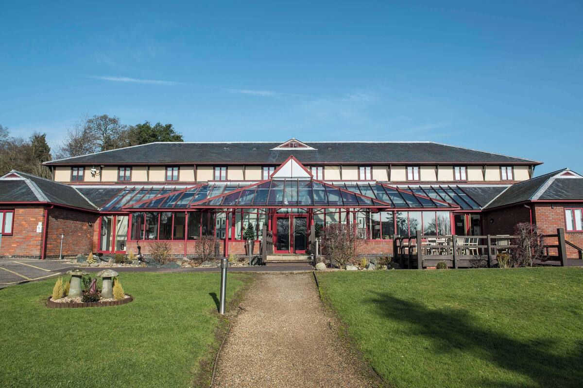 A building with a glass conservatory, a red entrance, and a gravel path leading to it.