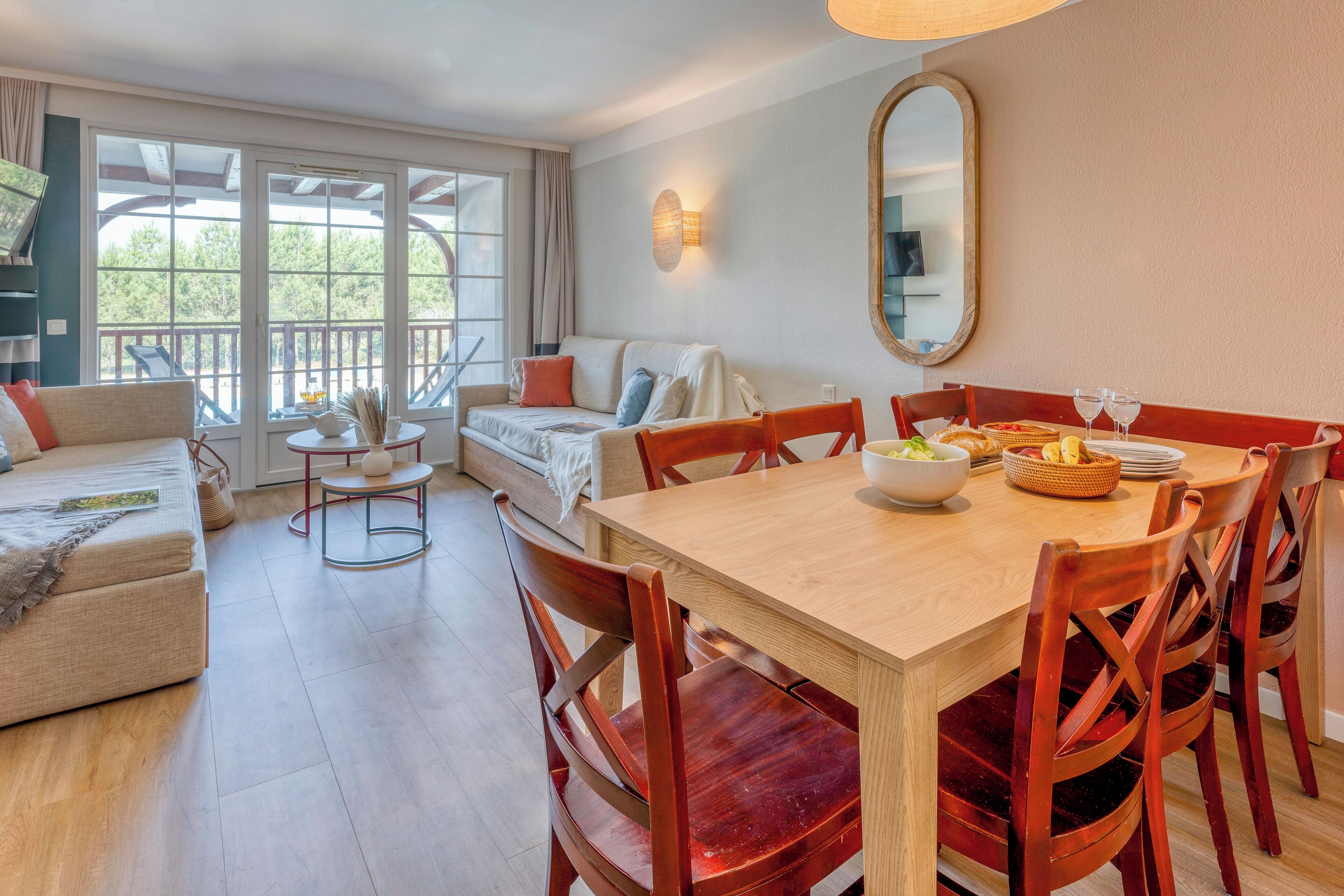 Un espace repas avec une table en bois, des chaises rouges et un canapé à l’arrière-plan.