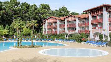 A hotel with a swimming pool, blue lounge chairs, and red balconies.