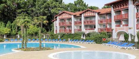 Un hôtel doté d’une piscine, de chaises longues bleues et de balcons rouges.