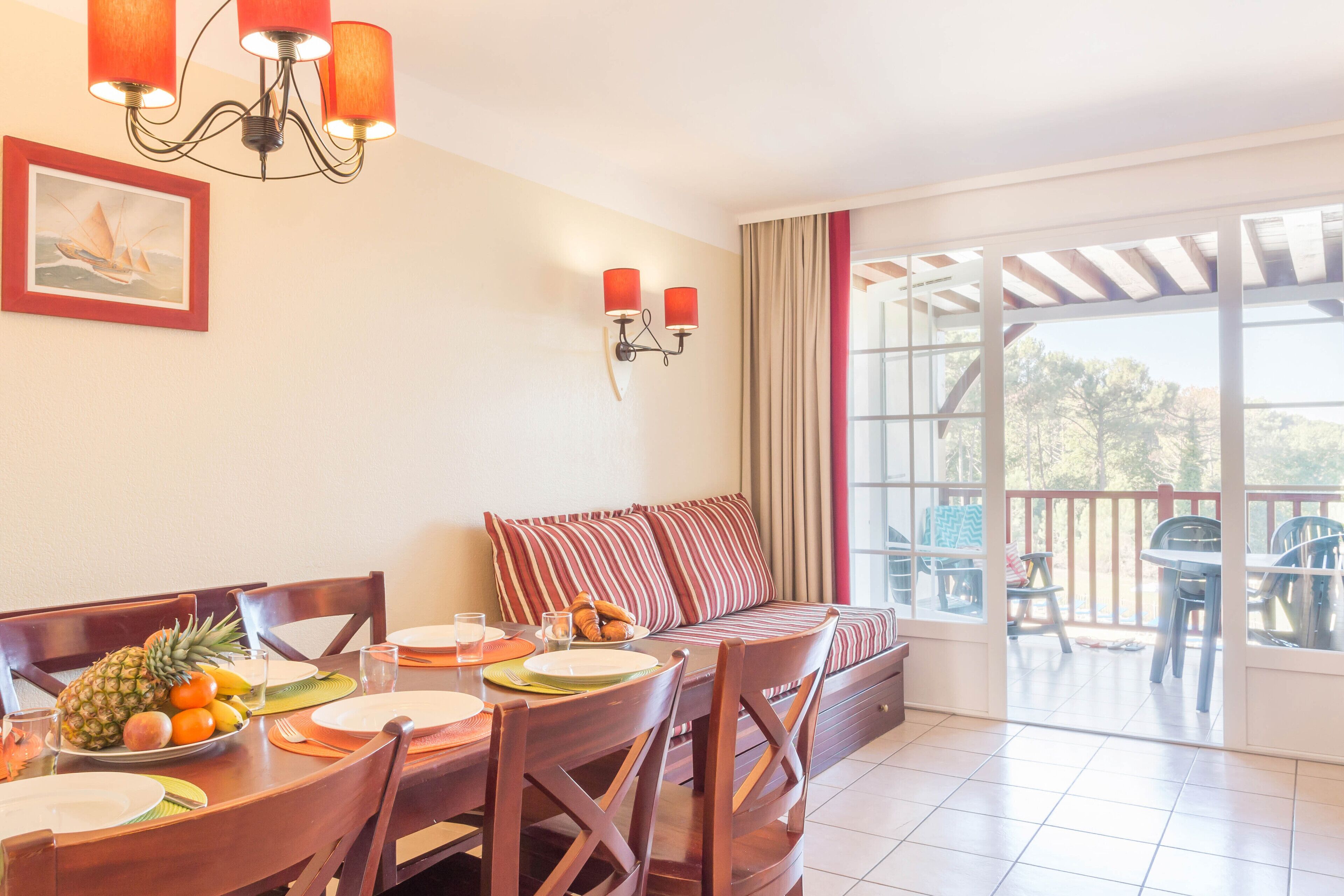 Un comedor con una mesa preparada para dos, un sofá con cojines a rayas y un balcón con mobiliario exterior.