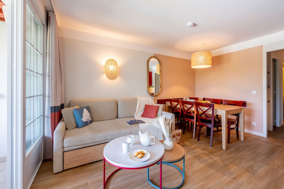 A modern living room with a sofa, a dining table, and chairs. There is a small round table with a teapot and cups.