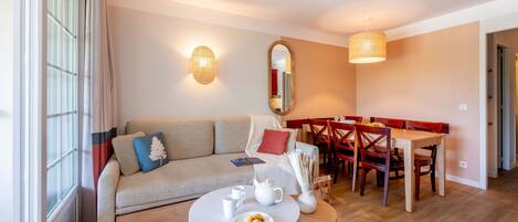 A modern living room with a sofa, a dining table, and chairs. There is a small round table with a teapot and cups.