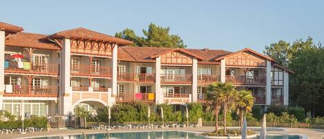 A hotel with multiple balconies, a swimming pool, and a fenced area with lounge chairs.