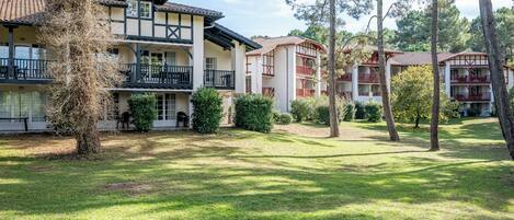 Um edifício com vários andares e varandas, rodeado por um gramado bem cuidado e árvores.
