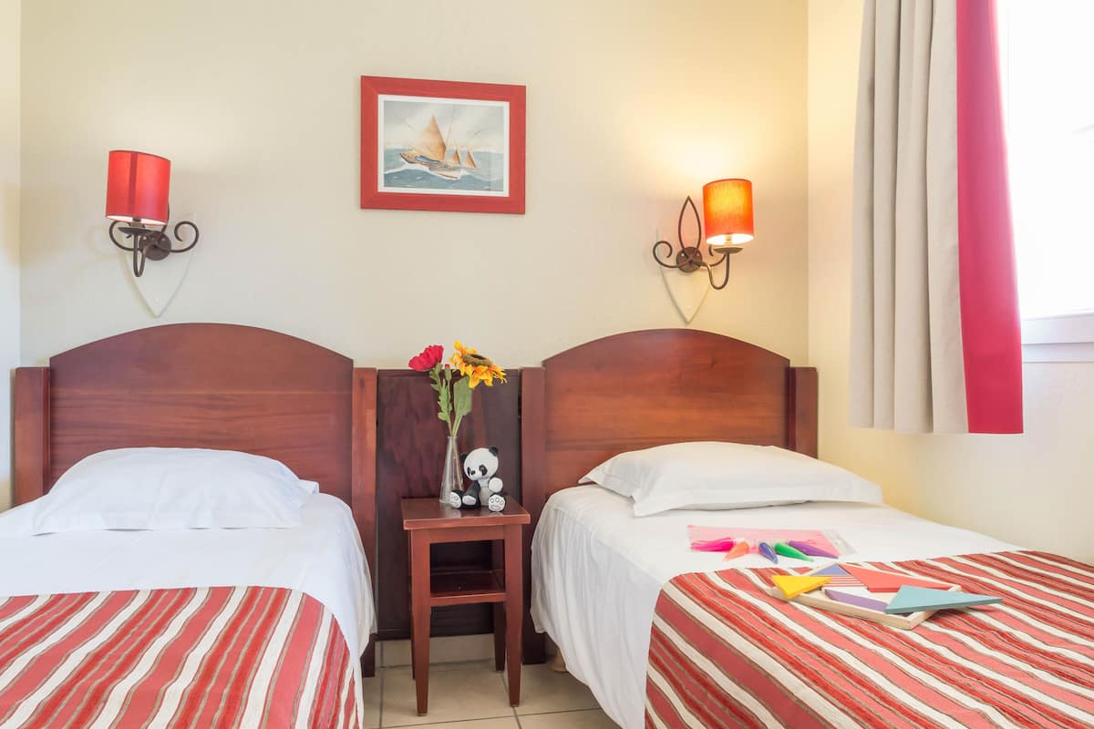 A hotel room with two beds, a nightstand, a vase with flowers, and wall-mounted lamps.