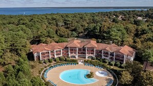 Ein Hotel mit Schwimmbecken, umgeben von Liegestühlen, in einer bewaldeten Gegend mit Blick auf das Meer.